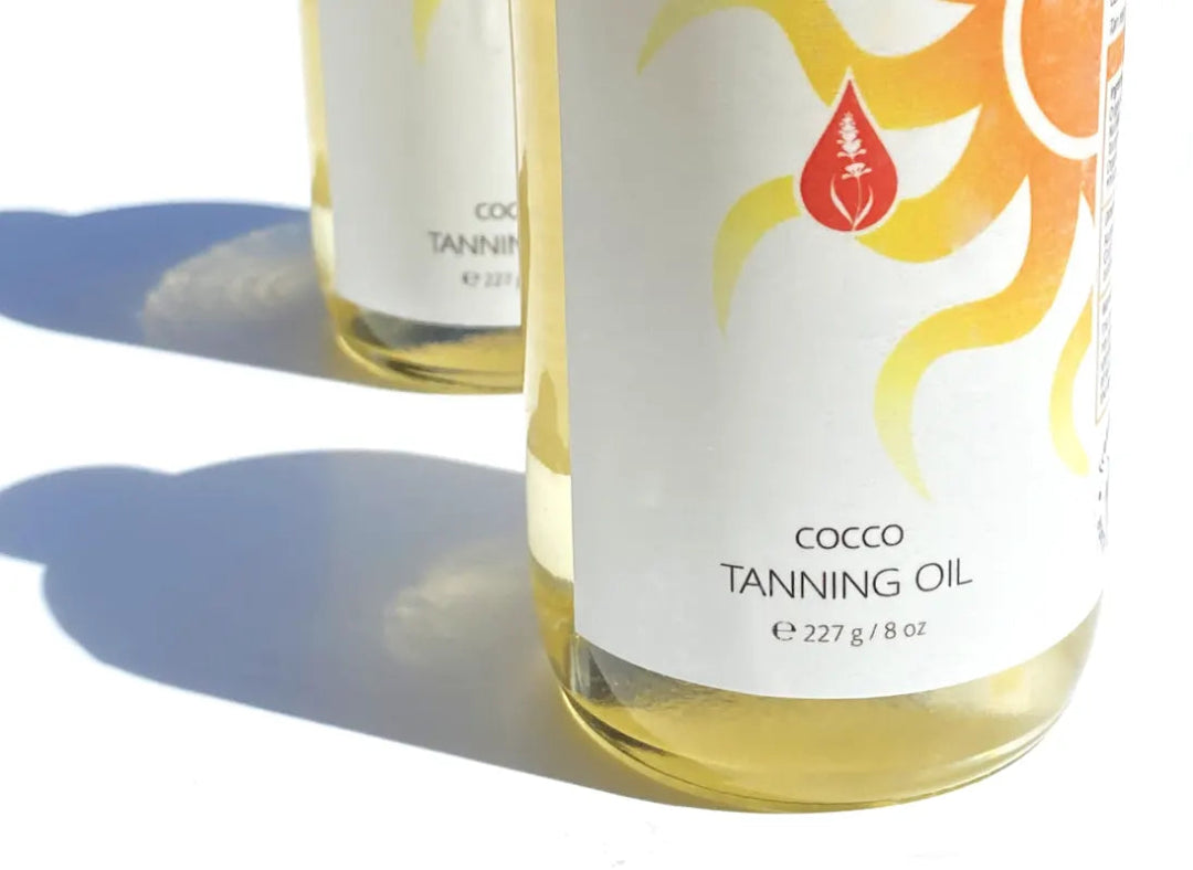 Close up of By Valenti Cocco Tanning Oil glass bottle and label casting a long afternoon shadow on a white background