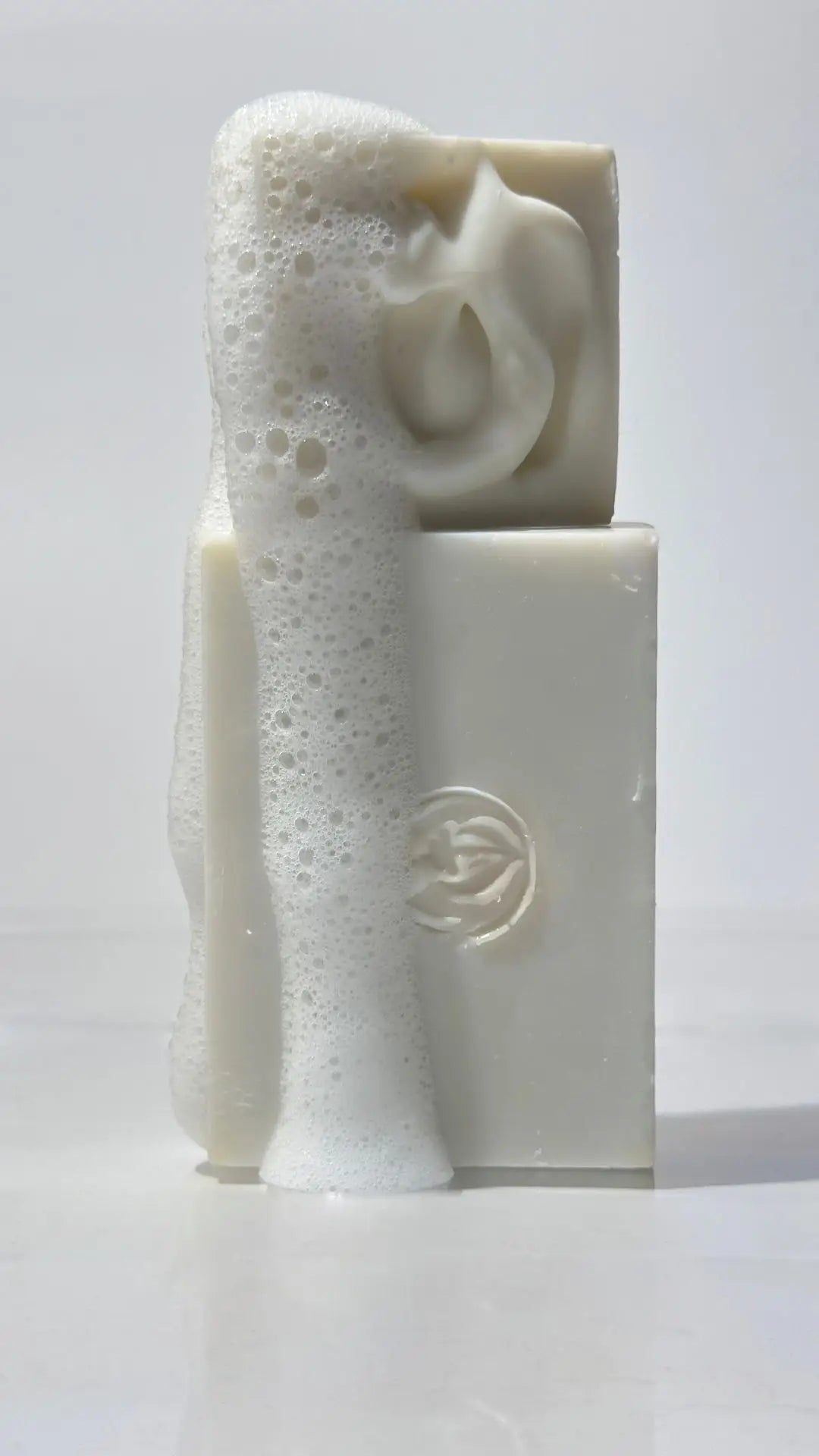 A full size and a travel size By Valenti Castile Bars of Soap with a foam on a white background