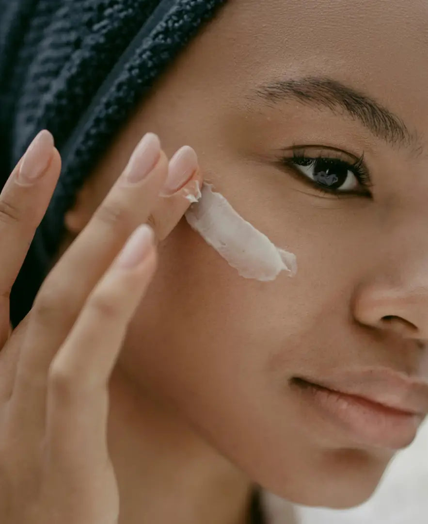 Woman applying cream to her face with a towel on her head