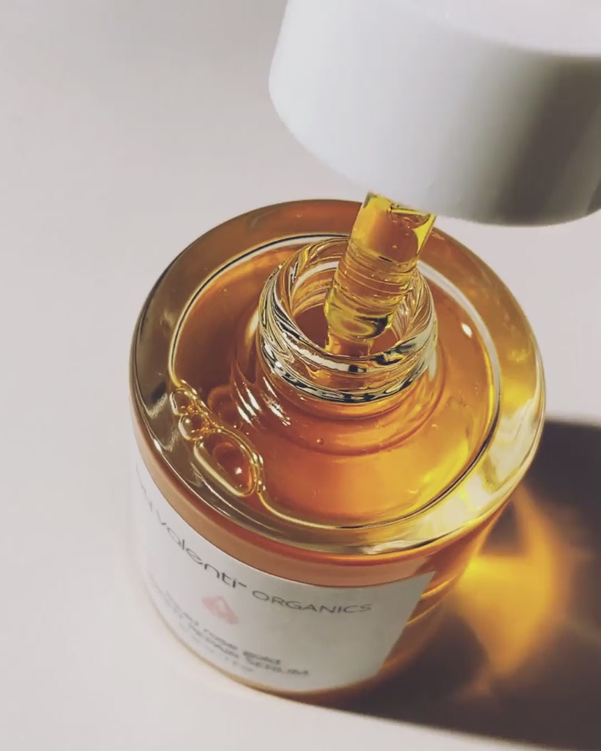 A bird eye shot of a glass dropper dripping By Valenti's orange/pink Liquid Rose Gold Night Repair Serum into the glass bottle on a white background